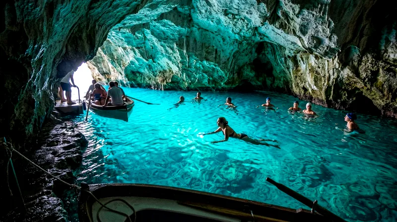 Visitors wading in the Blue Grotto's turquoise water with limestone cave walls and ceiling above